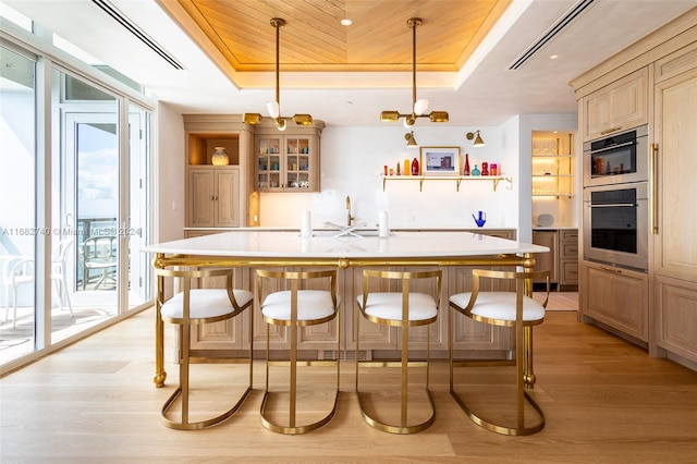 bar featuring light hardwood / wood-style flooring, a tray ceiling, light brown cabinets, and hanging light fixtures