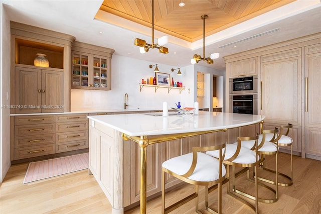 kitchen with a tray ceiling, a large island, a notable chandelier, decorative light fixtures, and light wood-type flooring