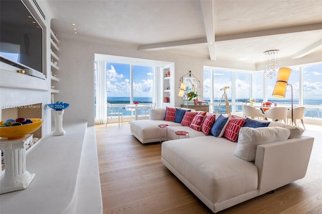 living room featuring beamed ceiling, a notable chandelier, a water view, and light wood-type flooring