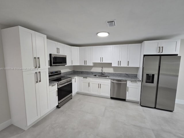 kitchen featuring appliances with stainless steel finishes, white cabinets, light stone countertops, and sink