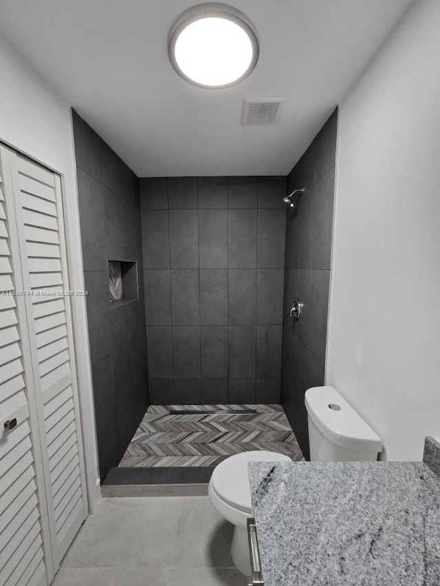 bathroom featuring vanity, tile patterned floors, a tile shower, and toilet