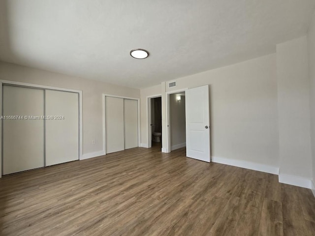 unfurnished bedroom featuring two closets and hardwood / wood-style floors