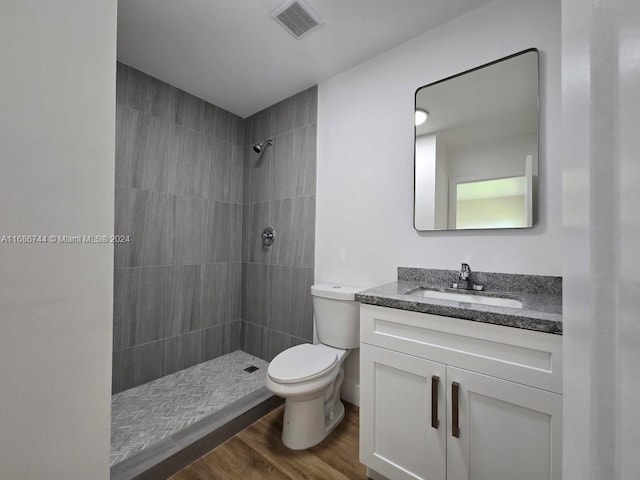 bathroom featuring vanity, hardwood / wood-style floors, toilet, and a tile shower