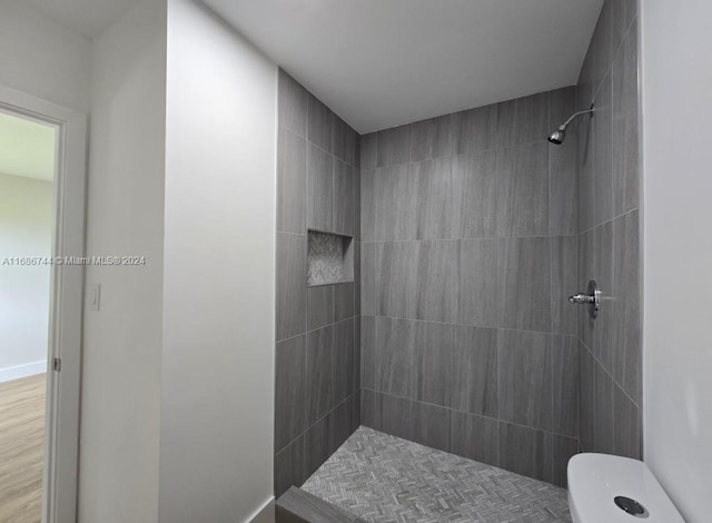 bathroom with tiled shower, hardwood / wood-style floors, and toilet