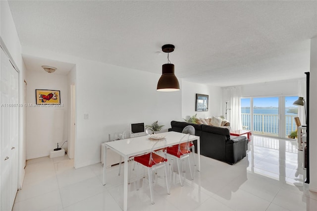 dining area featuring a textured ceiling, a water view, and light tile patterned floors