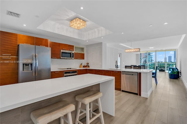 kitchen featuring appliances with stainless steel finishes, a raised ceiling, hanging light fixtures, expansive windows, and a breakfast bar