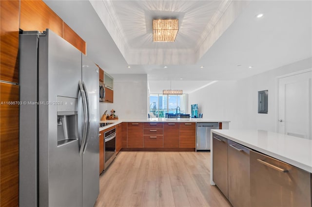 kitchen featuring sink, a tray ceiling, stainless steel appliances, light hardwood / wood-style flooring, and an inviting chandelier