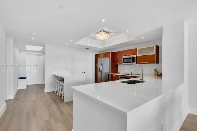 kitchen featuring kitchen peninsula, stainless steel appliances, light wood-type flooring, and a raised ceiling