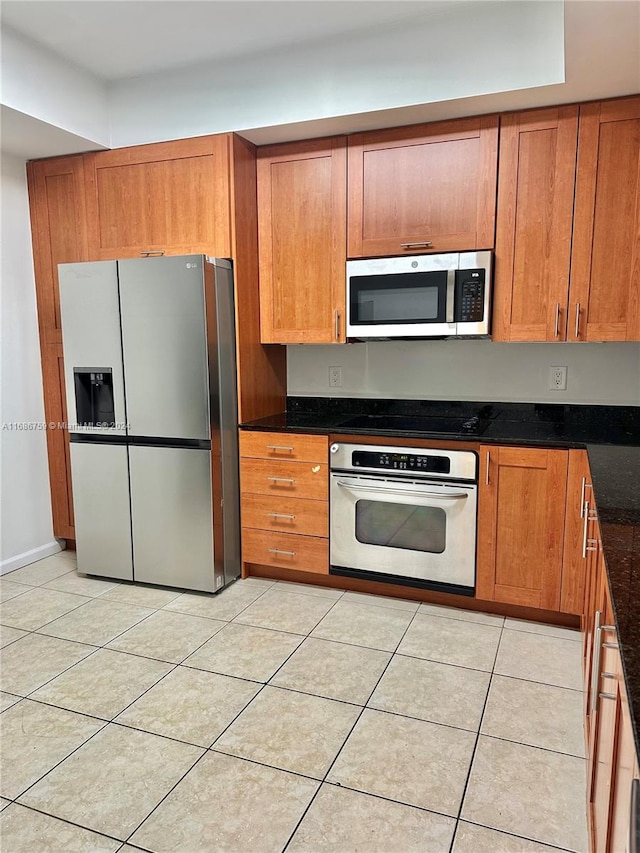 kitchen featuring appliances with stainless steel finishes, light tile patterned floors, and dark stone counters