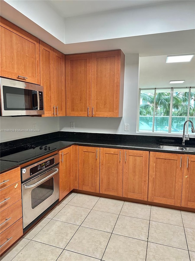 kitchen with light tile patterned floors, appliances with stainless steel finishes, sink, and dark stone counters