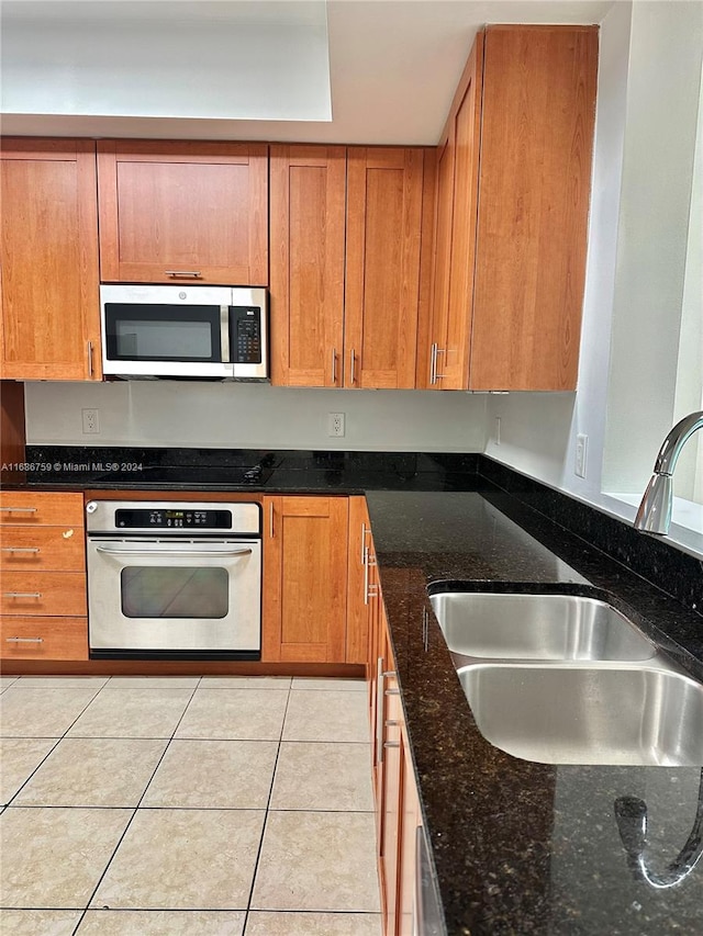 kitchen featuring sink, stainless steel appliances, light tile patterned floors, and dark stone counters