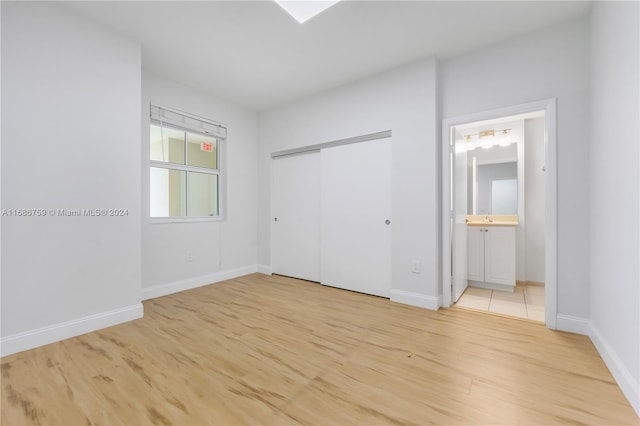 unfurnished bedroom featuring a closet, ensuite bathroom, and light hardwood / wood-style flooring