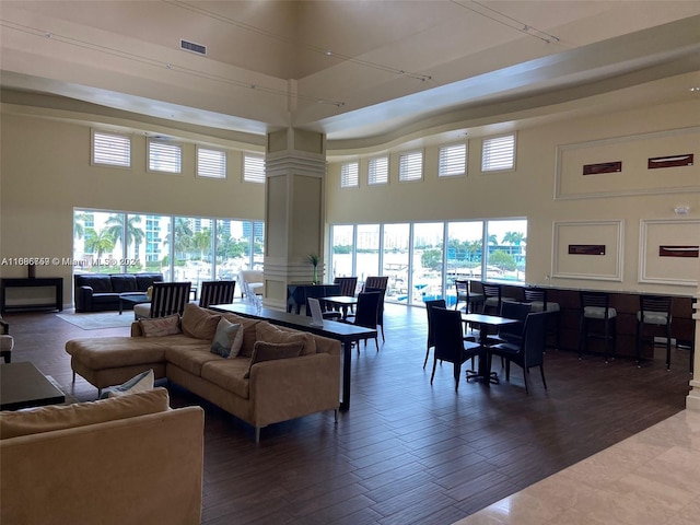 living room with dark wood-type flooring, a healthy amount of sunlight, a towering ceiling, and decorative columns