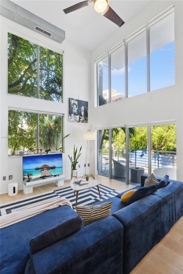 living room featuring a towering ceiling, ceiling fan, and light hardwood / wood-style flooring