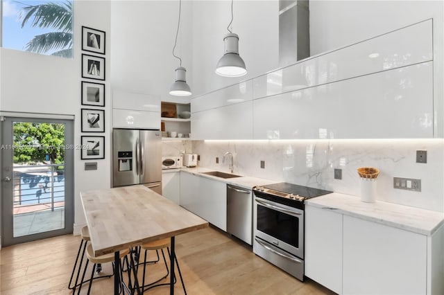 kitchen with white cabinetry, appliances with stainless steel finishes, decorative light fixtures, light wood-type flooring, and sink