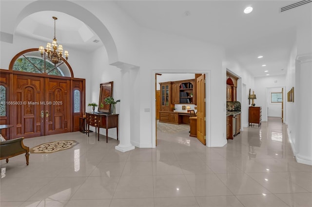 tiled foyer with ornate columns, a high ceiling, and a notable chandelier