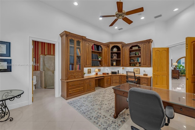 tiled office space with ceiling fan, built in desk, and a towering ceiling