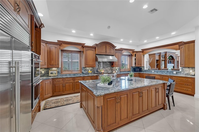 kitchen featuring stone counters, an island with sink, stainless steel appliances, and light tile patterned floors