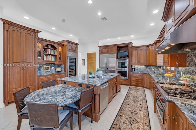 kitchen with light stone countertops, backsplash, premium appliances, ventilation hood, and a kitchen island