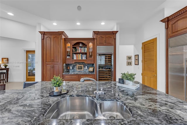 kitchen featuring sink, beverage cooler, backsplash, built in refrigerator, and dark stone counters