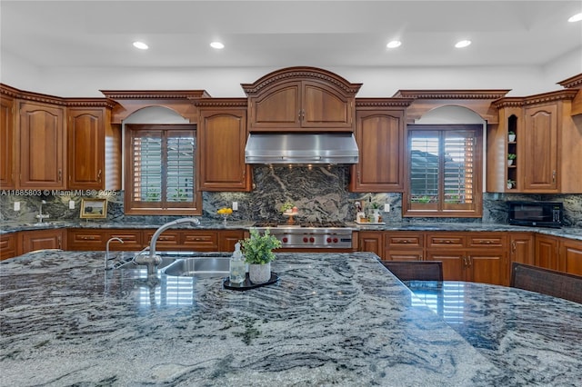 kitchen with stove, backsplash, dark stone counters, sink, and range hood