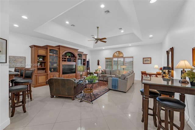 living room with a raised ceiling, ceiling fan, and light tile patterned floors