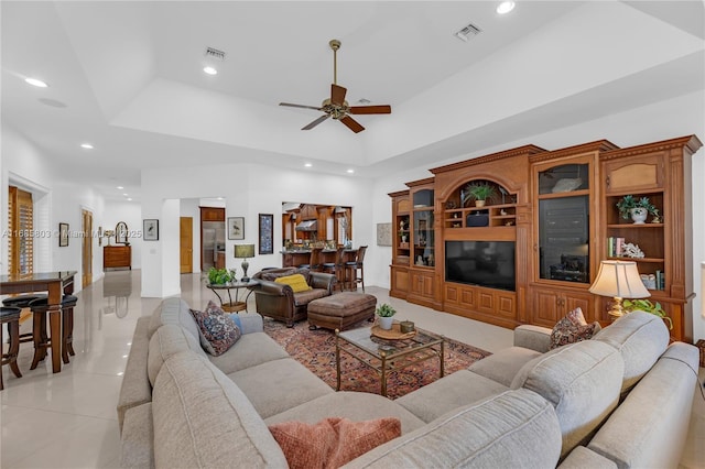 tiled living room featuring ceiling fan and a tray ceiling