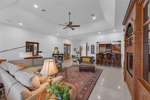 living room featuring a high ceiling, a tray ceiling, ceiling fan, and light tile patterned flooring