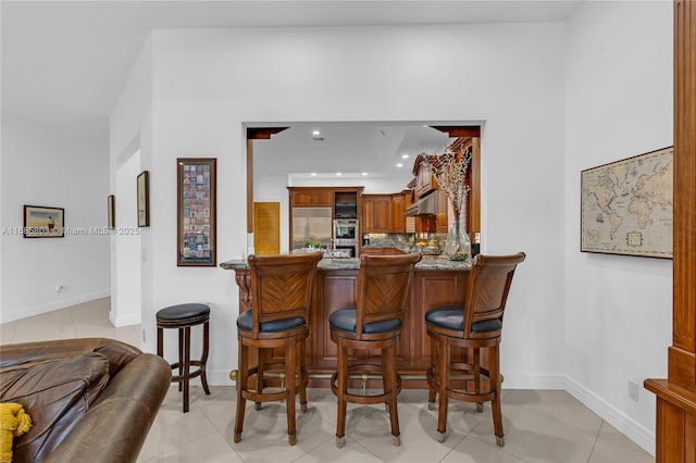 bar with stainless steel built in refrigerator, decorative backsplash, stone countertops, and light tile patterned flooring