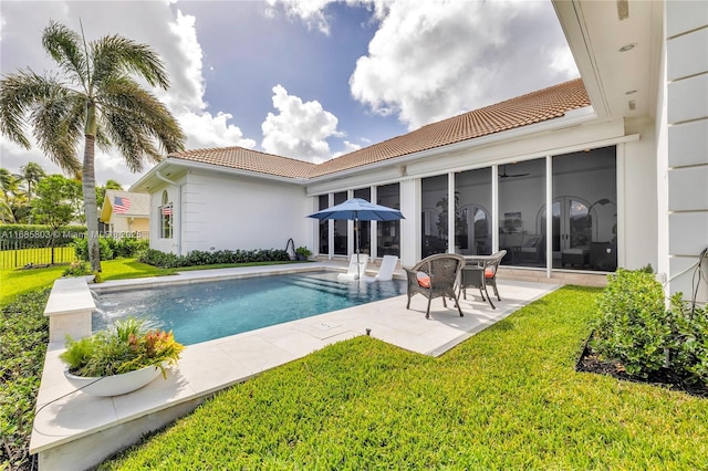 rear view of property featuring a fenced in pool, a lawn, and a sunroom