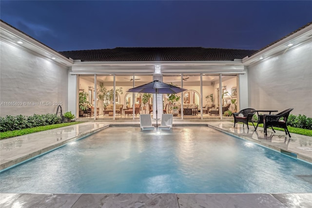 pool at night featuring pool water feature and a patio