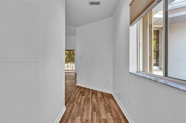 hallway with light wood finished floors, visible vents, and baseboards