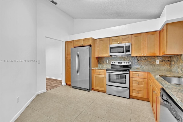 kitchen with decorative backsplash, lofted ceiling, appliances with stainless steel finishes, light stone countertops, and light tile patterned flooring