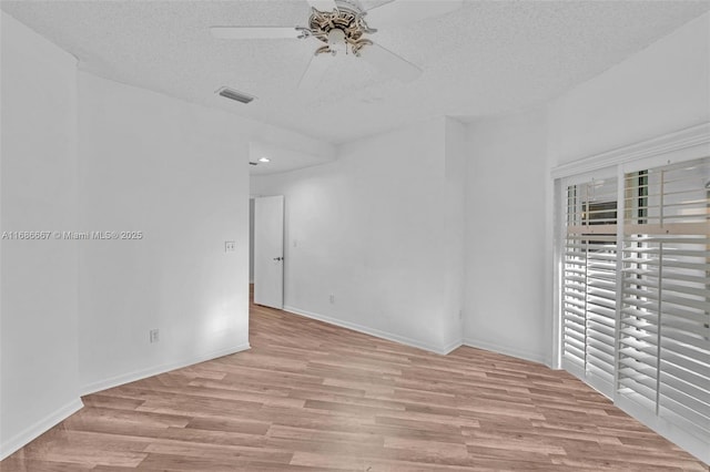 empty room with light wood-type flooring, visible vents, a textured ceiling, and baseboards