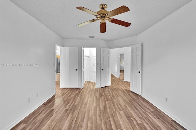 unfurnished bedroom featuring visible vents, light wood-style flooring, a spacious closet, a textured ceiling, and baseboards