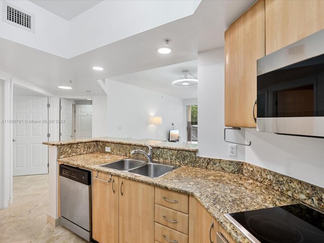 kitchen with stainless steel appliances, kitchen peninsula, sink, stone countertops, and light brown cabinets