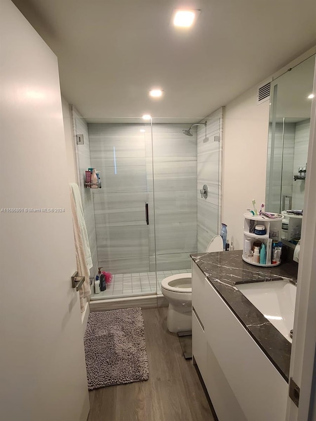 bathroom with toilet, hardwood / wood-style floors, vanity, and a shower with door