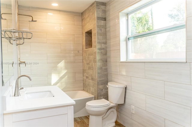 full bathroom featuring toilet, tiled shower / bath, vanity, and tile walls