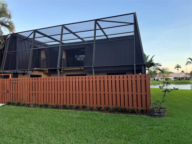 rear view of property with a yard, a water view, and glass enclosure