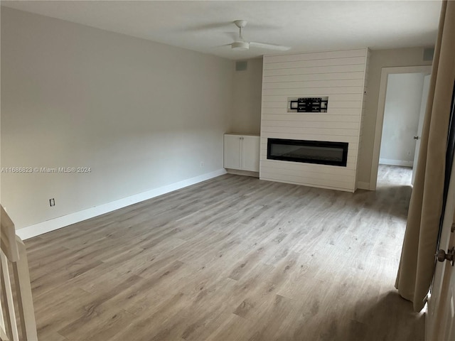 unfurnished living room with light hardwood / wood-style flooring, a large fireplace, and ceiling fan