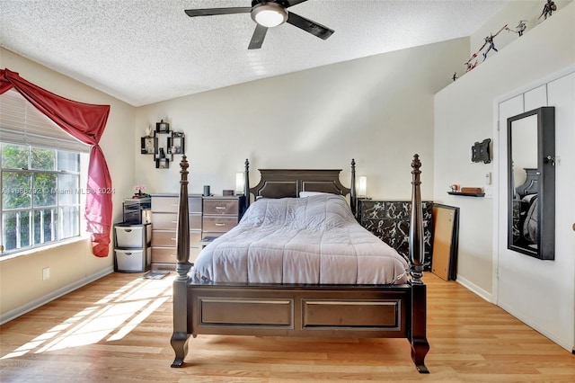 bedroom with ceiling fan, light hardwood / wood-style floors, lofted ceiling, and a textured ceiling