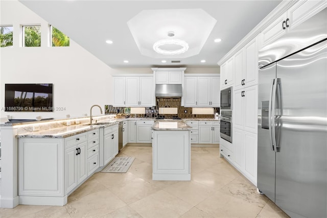 kitchen with built in appliances, light stone countertops, range hood, a kitchen island, and white cabinets