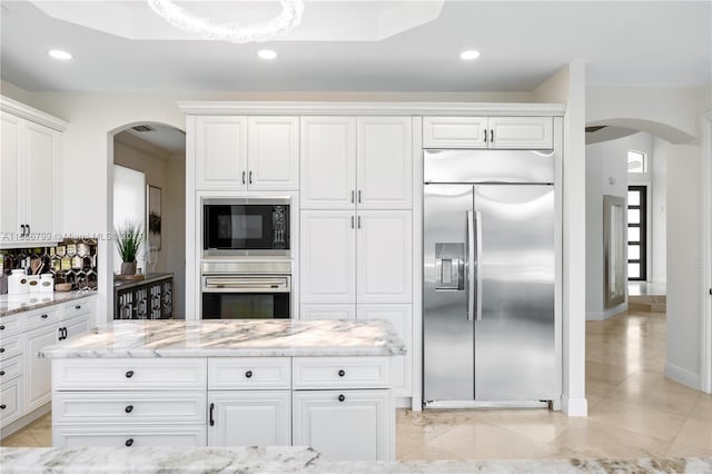 kitchen with light stone countertops, built in appliances, and white cabinets