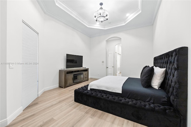 bedroom with light hardwood / wood-style floors, a raised ceiling, a chandelier, and crown molding