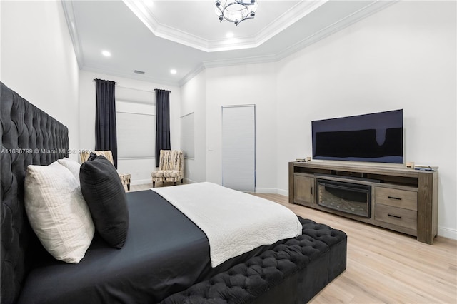 bedroom with a tray ceiling, an inviting chandelier, ornamental molding, and light hardwood / wood-style flooring