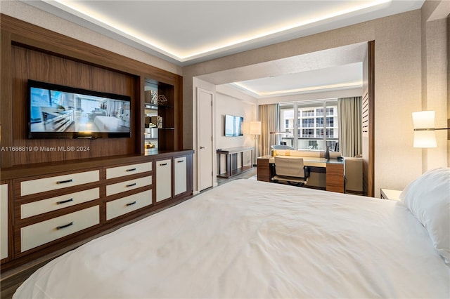 bedroom featuring built in desk, dark wood-type flooring, and a tray ceiling