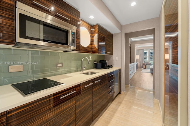 kitchen featuring black electric stovetop, light hardwood / wood-style flooring, sink, dark brown cabinetry, and tasteful backsplash