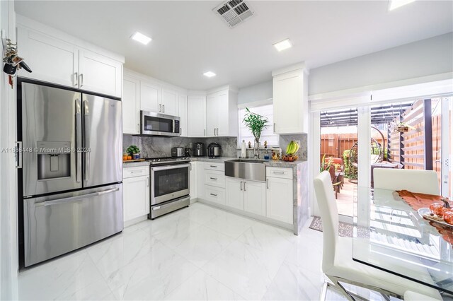 kitchen with white cabinetry, backsplash, stainless steel appliances, and sink