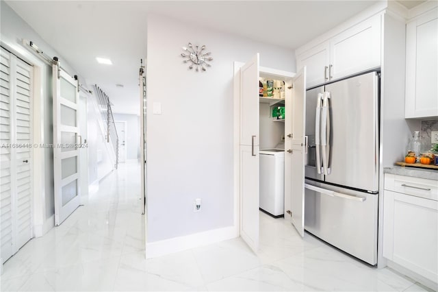 kitchen with stainless steel fridge, white cabinetry, a barn door, and washer / clothes dryer