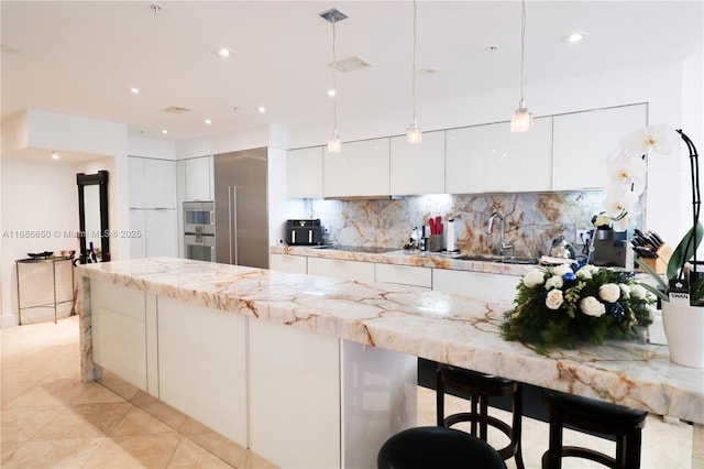 kitchen featuring light stone countertops, sink, hanging light fixtures, and white cabinets